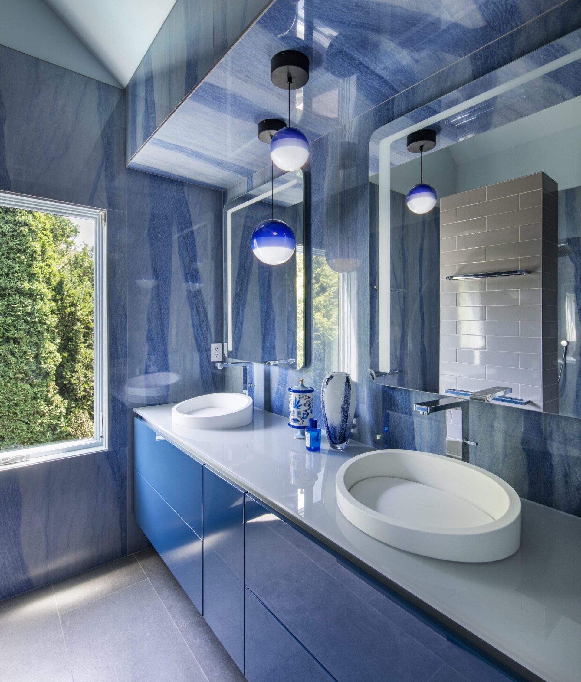 Interior of a home in Quincy, MA, designed by Ruhl Jahnes, showing the primary bathroom vanity with polished cobalt blue quartz wall slabs, a white vessel sink, floating blue cabinetry, globe pendant lights, and a large mirror.