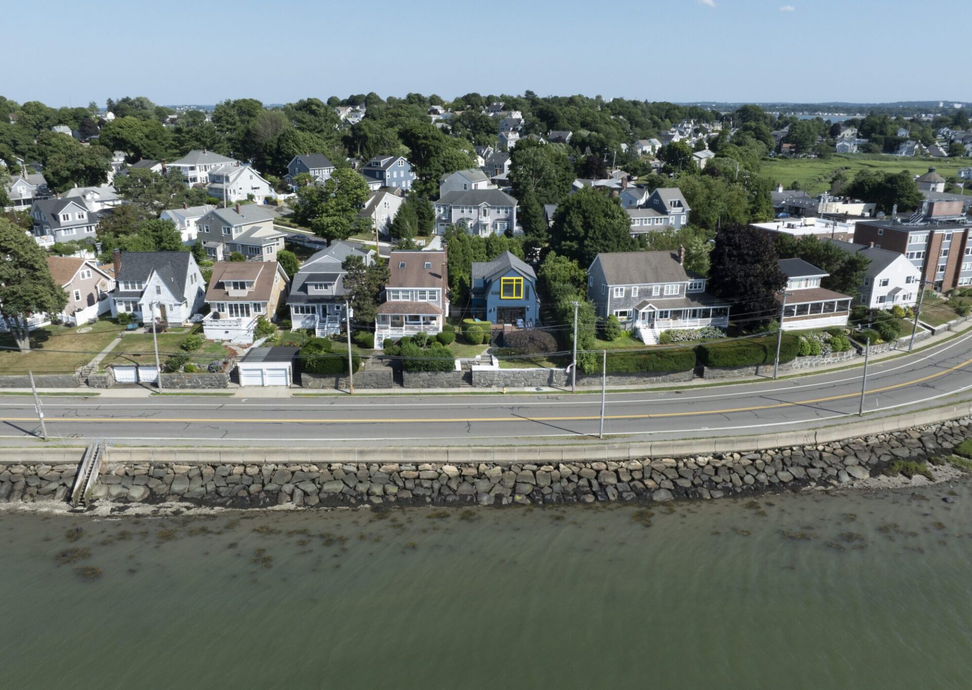 Aerial view of a neighborhood in Quincy, MA, showing a blue house designed by Ruhl Jahnes prominently sited among neighboring homes along the waterfront with Boston Harbor beyond.